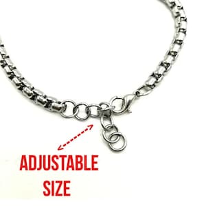 May include: A silver chain bracelet with an adjustable clasp. The bracelet is made of small, linked metal pieces. The clasp is a lobster claw style with a small chain attached to it. The text "ADJUSTABLE SIZE" is written below the bracelet.