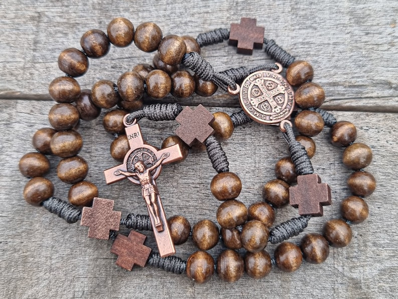 May include: A brown wooden rosary with a copper crucifix and a copper Saint Benedict medal. The rosary beads are strung on a black cord.
