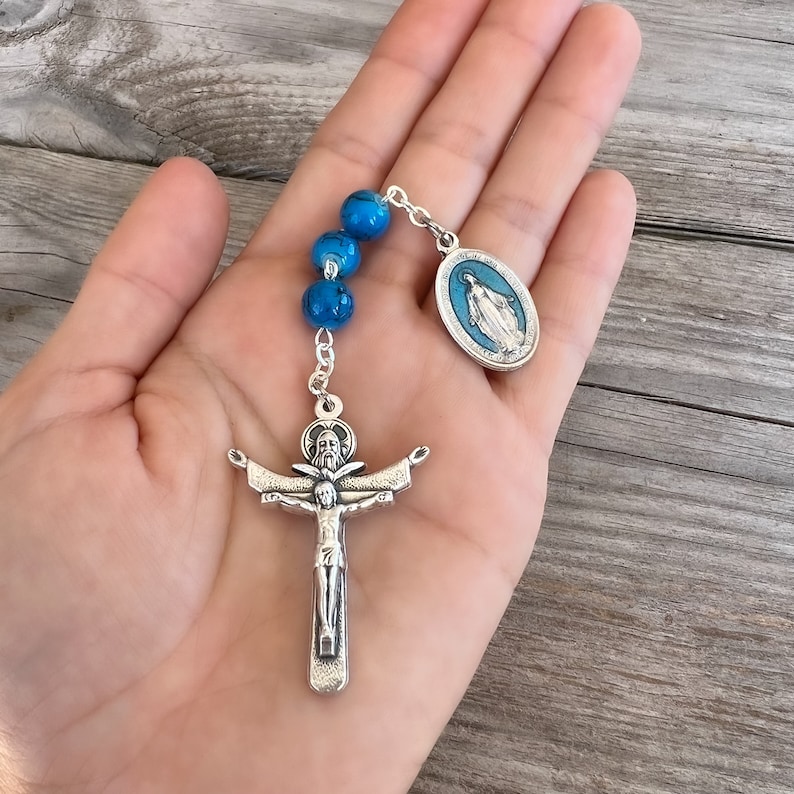 May include: A silver rosary with blue beads and a silver crucifix. The crucifix features a depiction of Jesus Christ. The rosary also includes a silver charm with a depiction of the Virgin Mary.