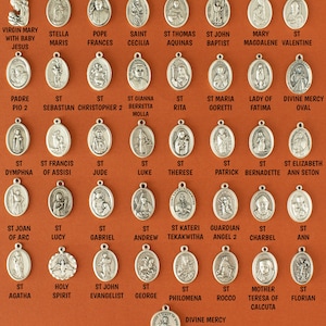 May include: A collection of silver oval-shaped medallions with various religious figures and names. The medallions are arranged in rows on a brown background.