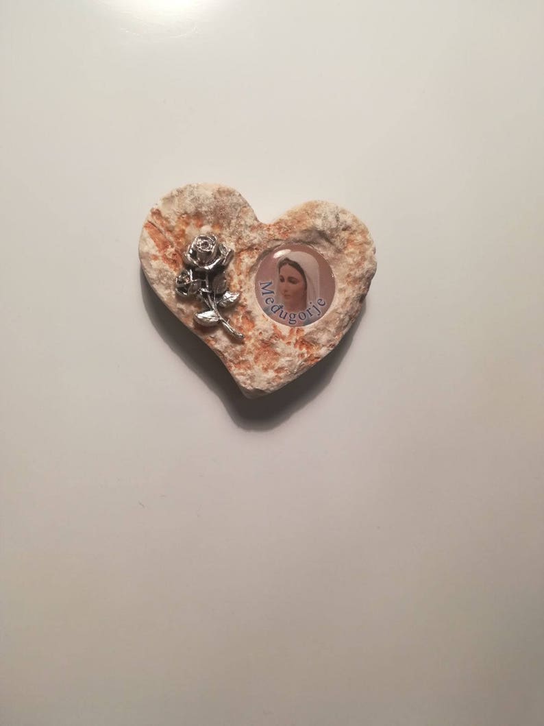 K&ouml;nnte beinhalten: Ein herzf&ouml;rmiger Stein mit einem Bild der Jungfrau Maria und dem Wort "Medjugorje" darin. Eine silberne Rose ist an der Seite des Herzens befestigt.