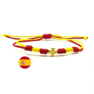 May include: Red and yellow braided bracelet with a gold cross charm. The bracelet is tied with a knot and has a sliding knot for adjusting the size. The bracelet is accented with the Spanish flag.
