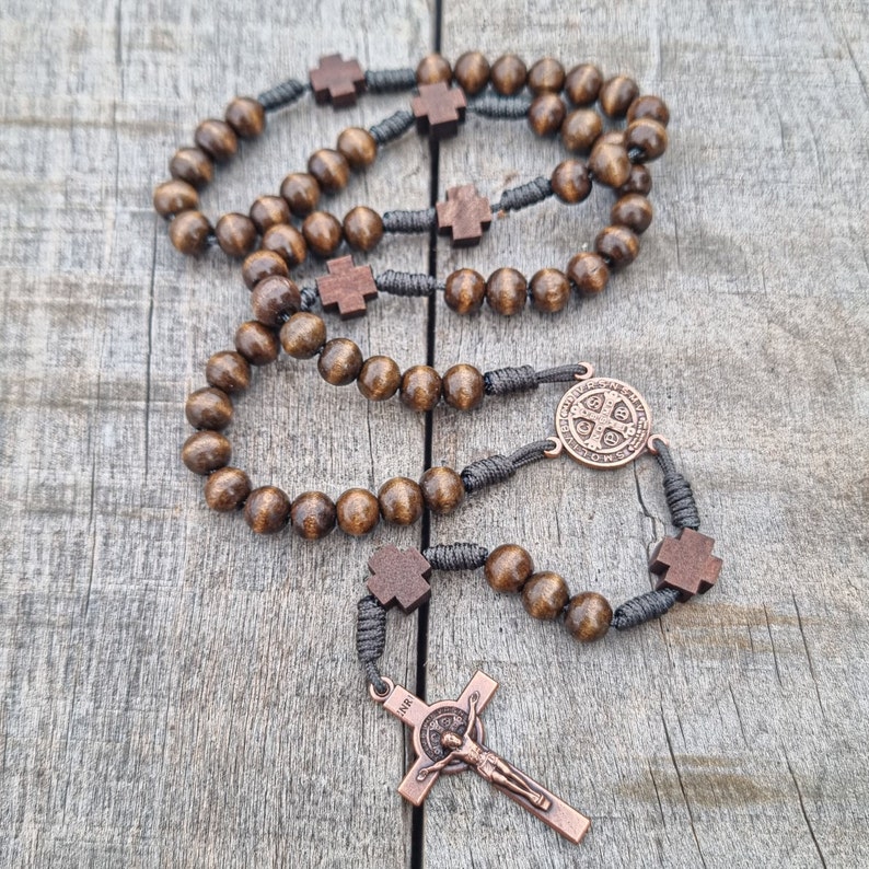 May include: A brown wooden rosary with a black cord and a copper St Benedict medal and crucifix.