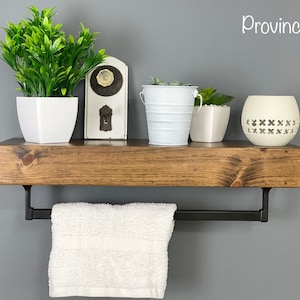 May include: A rustic wooden shelf with a black metal towel bar, featuring a white towel, potted plants, and a decorative white candle holder. The shelf is labeled "Provincial".