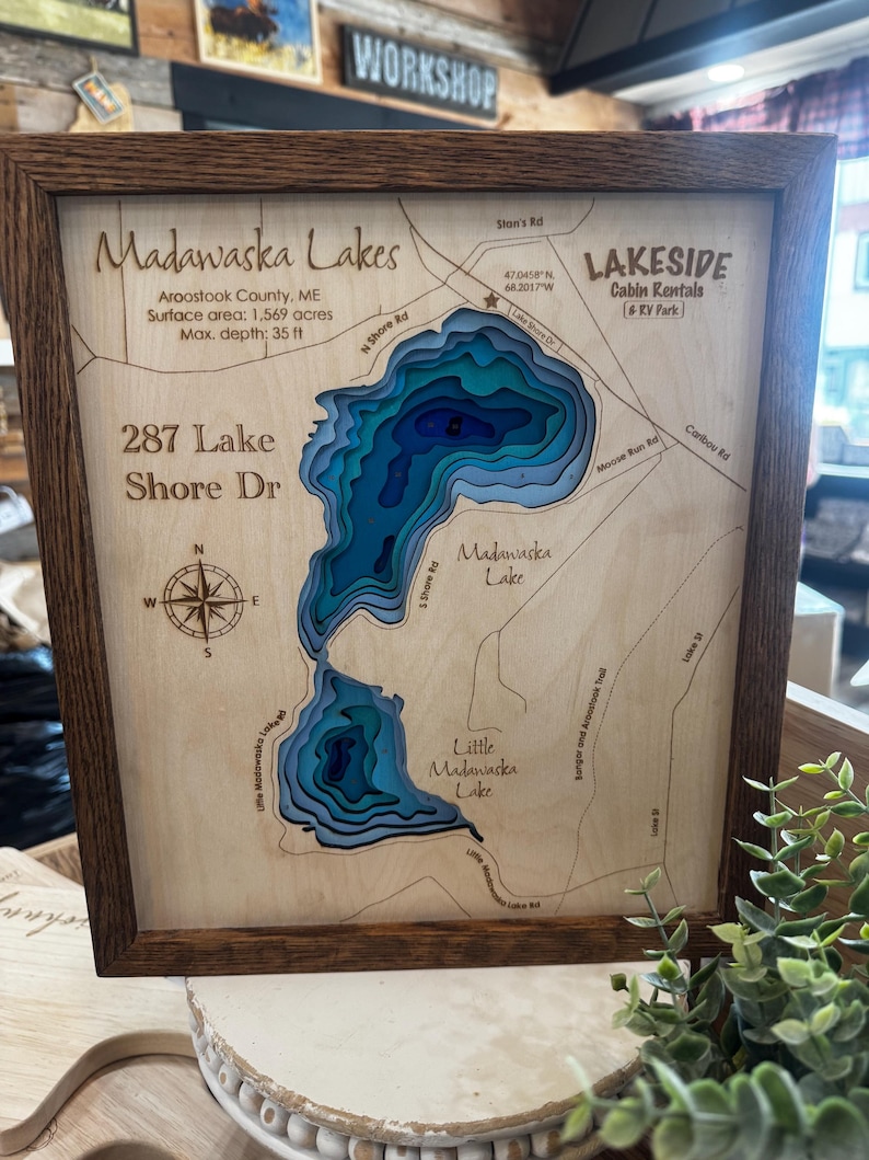 Puede incluir: Mapa de los lagos Madawaska, Maine, cortado con l&aacute;ser y enmarcado en madera, con contornos de profundidad en tonos azules. Incluye el texto: "287 Lake Shore Dr" y "Lakeside Cabin Rentals". La profundidad m&aacute;xima es de 10,67 metros.