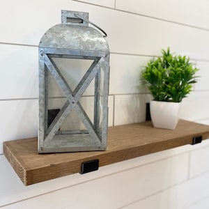 May include: A rustic wooden shelf with black metal brackets, featuring a galvanized metal lantern and a potted green plant.
