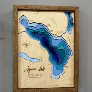 Puede incluir: Un mapa de madera enmarcado del lago Square en el condado de Aroostook, ME. El mapa presenta contornos azules y celeste en capas que representan la profundidad del lago. El texto incluye el nombre del lago, la superficie y una profundidad m&aacute;xima de 37,18 m.