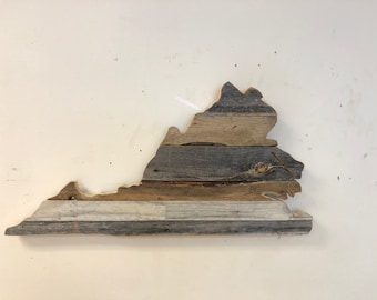 Puede incluir: Una pieza de arte de pared de madera con la forma del estado de Virginia. La madera es una mezcla de marrón claro y oscuro, gris y blanco. La madera está desgastada y tiene un aspecto rústico.