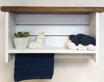 May include: White wooden shelf with a brown top, featuring a white unicorn figurine, a potted succulent, and rolled towels. The shelf has a towel bar underneath.