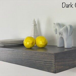 May include: Dark gray floating shelf with a white ceramic tower, two yellow lemons, and a gray ceramic unicorn figurine with the word "Spirit" written on it.