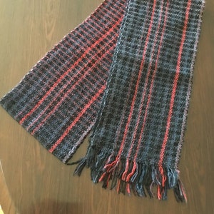 May include: A black and red striped woven scarf with fringe on the ends.