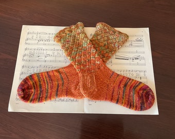 May include: A pair of orange and brown striped socks with a green and brown pattern at the top. The socks are laid out on a sheet of music.