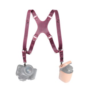 A purple leather camera strap with two camera attachments hanging from it.