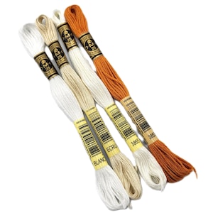 May include: Four spools of embroidery floss in white, cream, and orange. The spools are labeled with the DMC brand name and color numbers: "BLANC", "ECRU", "3865", and "3863".