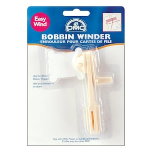 May include: A DMC Bobbin Winder for winding thread and ribbon. The package is blue and white, with the words "Easy Wind" in a red circle. The winder is a light beige color and is designed to work with DMC plastic or cardboard bobbins.