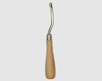 May include: A rug hooking tool with a curved, silver-colored metal hook and a light brown wooden handle. The handle is smooth and rounded, providing a comfortable grip for detailed craft work.