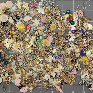 May include: A large collection of colorful enamel pins featuring various designs, including animals, flowers, and geometric shapes. The pins are arranged in a random pattern on a gray surface.