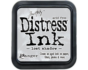 May include: A black ink pad with the text "Distress Ink - lost shadow -" and the brand name "Ranger" printed on it. The ink pad is acid free and is designed to create an aged look on papers, fibers, photos, and more.