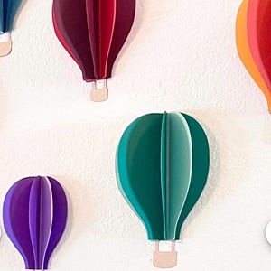 May include: A collection of colorful paper hot air balloons with different shades of blue, red, green, purple, and orange. The balloons are all the same size and shape, and they are hanging from the ceiling.