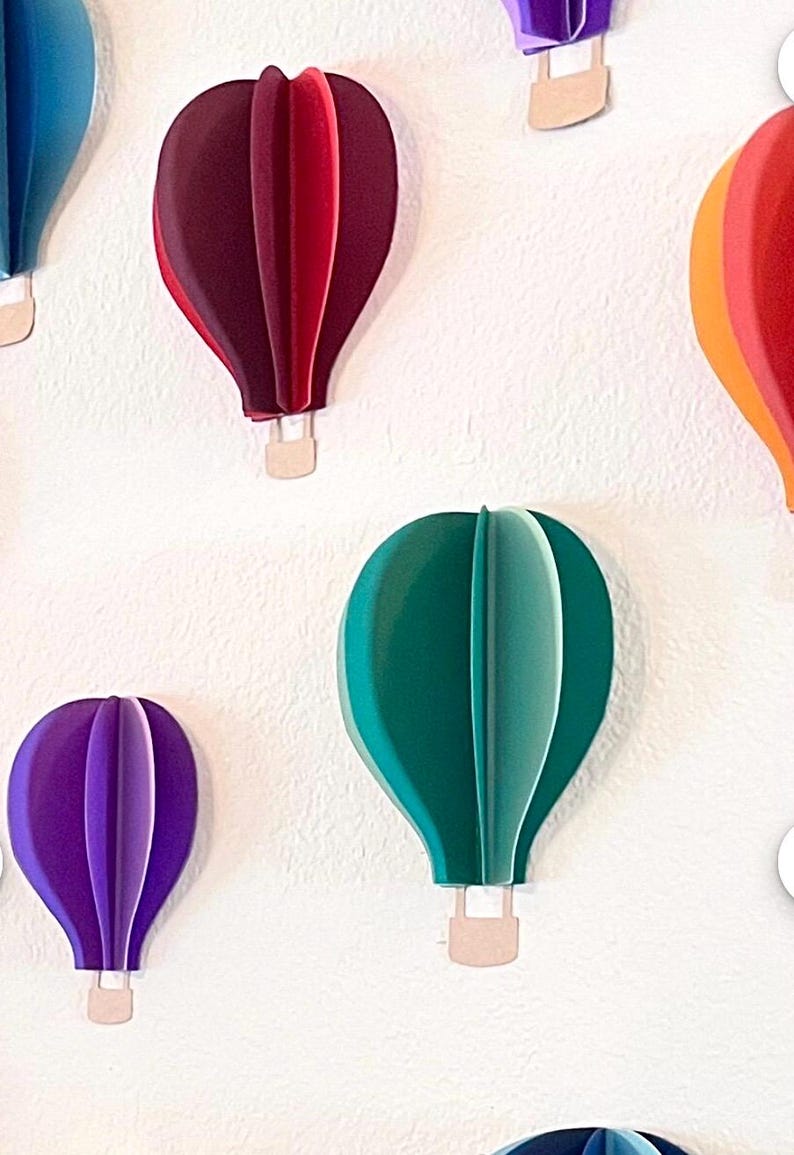 May include: A collection of colorful paper hot air balloons with different shades of blue, red, green, purple, and orange. The balloons are all the same size and shape, and they are hanging from the ceiling.