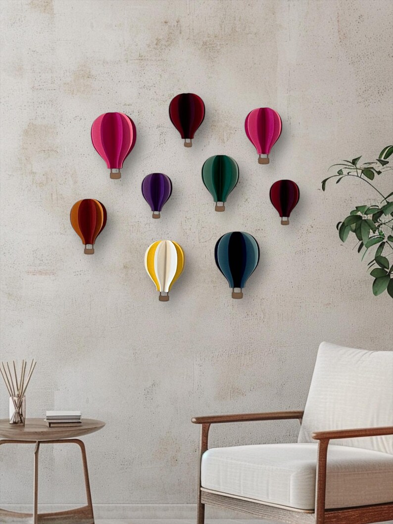 May include: A wall decor set of nine paper hot air balloons in various colors, including red, pink, purple, green, yellow, and blue. The balloons are arranged in a staggered pattern on a light gray wall.