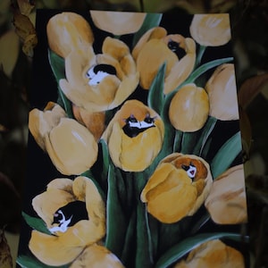 May include: A painting of yellow tulips with black and white cats sleeping inside them. The tulips are arranged in a bouquet and the background is black.