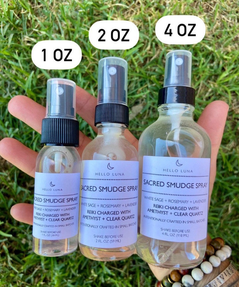 May include: Three glass spray bottles with black tops and labels that say "Hello Luna Sacred Smudge Spray". The bottles are labeled with different sizes: 1 oz, 2 oz, and 4 oz. The bottles are filled with a clear liquid.