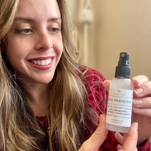 May include: A clear glass bottle with a black spray nozzle and a white label. The label says "Hello Luna Sacred Smudge Spray White Sage + Rosemary + Lavender Reiki Charged with Amethyst + Clear Quartz Handcrafted in Small Batches Shake Before Use 1 fl oz (29 ml)"