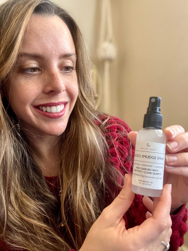 May include: A clear glass bottle with a black spray nozzle and a white label. The label says "Hello Luna Sacred Smudge Spray White Sage + Rosemary + Lavender Reiki Charged with Amethyst + Clear Quartz Handcrafted in Small Batches Shake Before Use 1 fl oz (29 ml)"