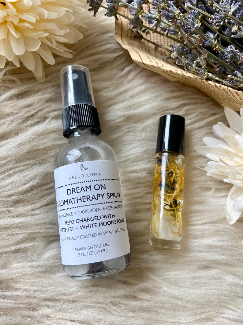 Puede incluir: Se muestran dos productos de aromaterapia: un frasco de spray transparente y un peque&ntilde;o frasco roll-on. El frasco de spray tiene una tapa negra y una etiqueta con el texto "Dream On Aromatherapy Spray". El roll-on contiene elementos bot&aacute;nicos visibles.