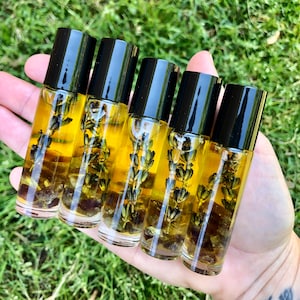 May include: Five small glass bottles with black roll-on tops filled with a clear yellow liquid and dried lavender flowers. The bottles are arranged in a row on a hand.