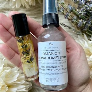 Puede incluir: Se muestran dos productos de aromaterapia: un frasco roll-on y un frasco en spray. El roll-on contiene elementos bot&aacute;nicos visibles. El frasco en spray, etiquetado como "Dream On Aromatherapy Spray", es de 59 ml y contiene manzanilla y lavanda.