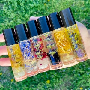 May include: Six small glass bottles with black caps filled with clear liquid and dried flowers and crystals. The bottles are arranged in a row from left to right, with the largest bottle on the left and the smallest bottle on the right.