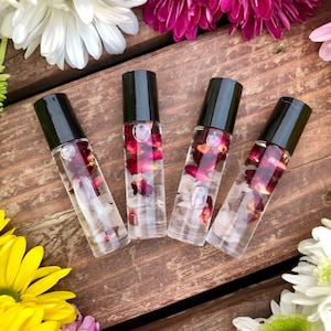May include: Four clear glass roller bottles with black caps filled with a clear liquid and rose petals. The bottles are arranged in a row on a wooden surface.