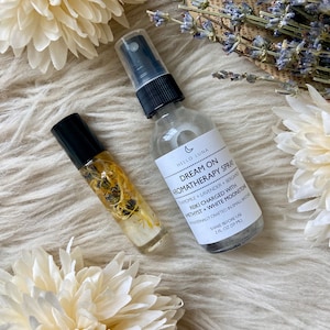 Puede incluir: Productos de aromaterapia, que incluyen un frasco rociador y un frasco roll-on, se exhiben sobre una superficie blanca texturizada. El frasco rociador tiene una tapa negra y una etiqueta que dice "Dream On Aromatherapy Spray". El frasco roll-on contiene elementos bot&aacute;nicos visibles.
