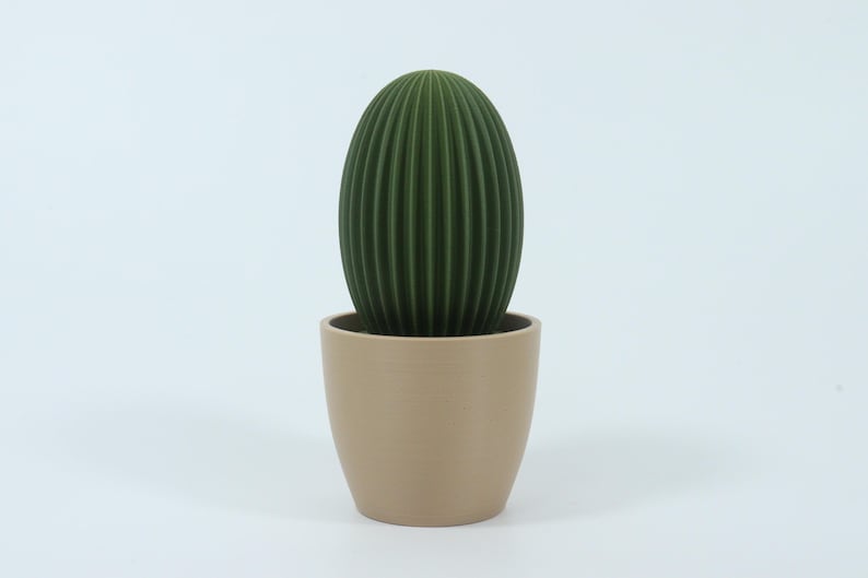 May include: A green, ribbed cactus-shaped decorative item in a beige pot. The cactus has a vertical, oval shape with detailed ridges. The pot is a simple, cylindrical design. The background is plain white.