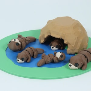 Puede incluir: Cinco figuritas de nutria marrón están dispuestas en una alfombra de juego verde y azul. Una nutria está dentro de una estructura de cueva marrón. Las nutrias están todas en diferentes poses.