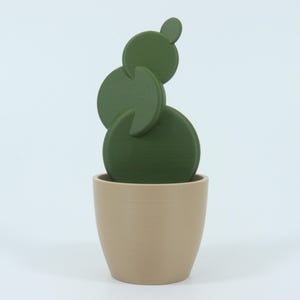 May include: A decorative cactus sculpture in a beige pot. The cactus is composed of several green, circular shapes stacked on top of each other. The pot is a simple, rounded design.