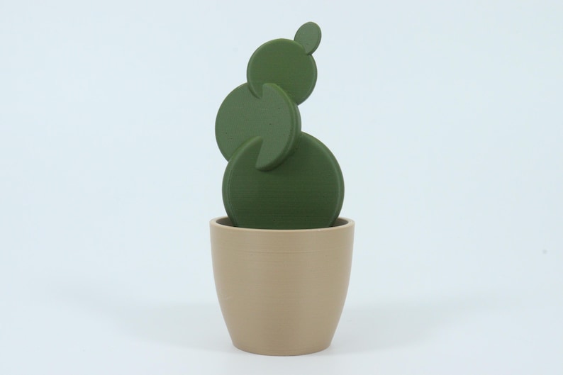 May include: A decorative cactus sculpture in a beige pot. The cactus is composed of several green, circular shapes stacked on top of each other. The pot is a simple, rounded design.