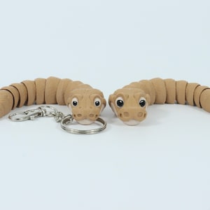 May include: Two brown segmented snake-shaped keychains with cartoon faces and black eyes. The keychains are connected to a silver key ring.