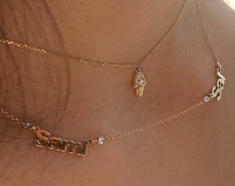 May include: Two gold necklaces with a hamsa hand charm and the name "Sami" on one necklace.