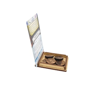 May include: A wooden box with a hinged lid, open to reveal four wooden tokens with intricate designs. The box has a card inside with text that reads "The Prophecy of the Seer".