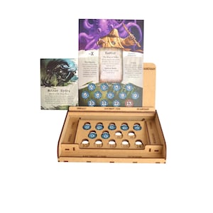 Könnte beinhalten: Ein Brettspiel-Organizer aus Holz mit kreisförmigen Aussparungen für Spielsteine und einem vertikalen Kartenhalter, der eine Bastur-Charakterkarte und eine Mother Hydra-Karte zeigt. Der Organizer enthält nummerierte Fächer und blaue Spielsteine.