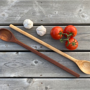 May include: Two wooden spoons, one brown and one natural wood, on a wooden surface with three garlic cloves and four red tomatoes.