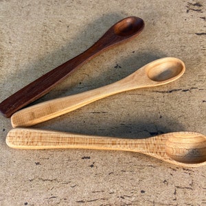 May include: Three wooden spoons, two are light brown and one is dark brown. The spoons are arranged in a row on a light brown textured surface.