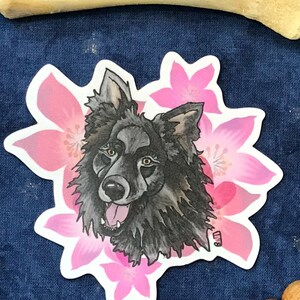 Puede incluir: Una ilustración en blanco y negro de la cabeza de un perro con un fondo floral rosa. El perro tiene la nariz y la lengua negras, y sus ojos son marrones. Las flores son rosas y blancas.