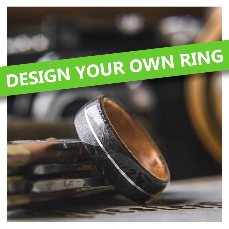 May include: A black and silver ring with a wood inlay. The ring is on a table with a blurred background. The text "DESIGN YOUR OWN RING" is in the background.
