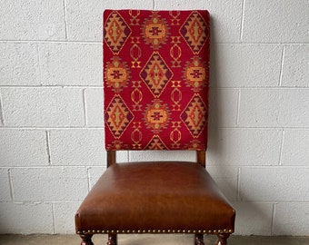 May include: A wooden chair with a brown leather seat and a red, yellow, and orange patterned back. The chair has a twisted design on the legs.