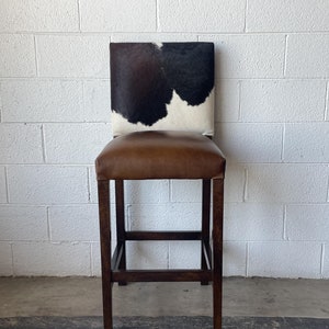 May include: A brown leather bar stool with a black and white cowhide seat.