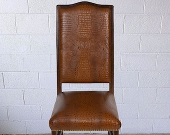 May include: A brown leather chair with a high back and a crocodile skin pattern. The chair has a dark wooden frame and is set against a white brick wall.